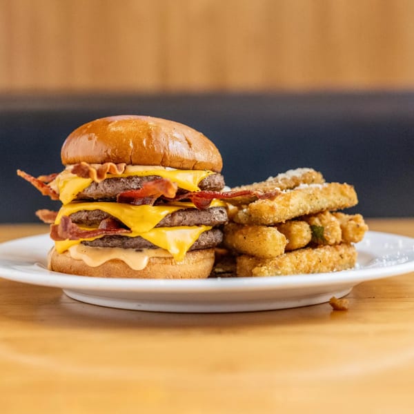 A triple bacon cheeseburger with melted cheese and a side of crispy fries on a white plate.
