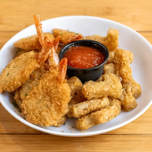 A white bowl filled with golden-brown fried shrimp and fried cheese curds, with a side of red dipping sauce.