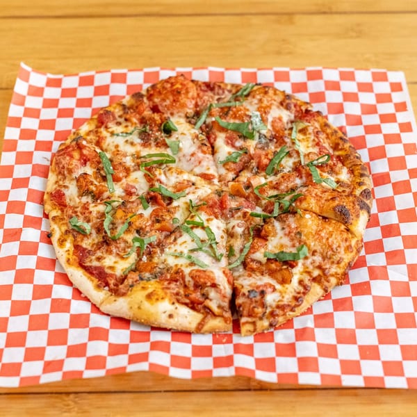 A Beach Sports Grill & Bar pizza with cheese, sauce, and basil on red and white checkered paper.