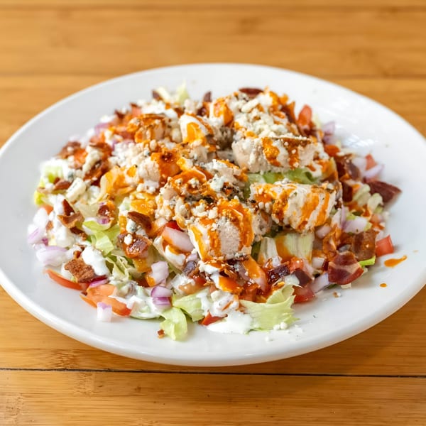 Buffalo chicken salad with bacon, blue cheese, red onion, and tomatoes on a white plate.