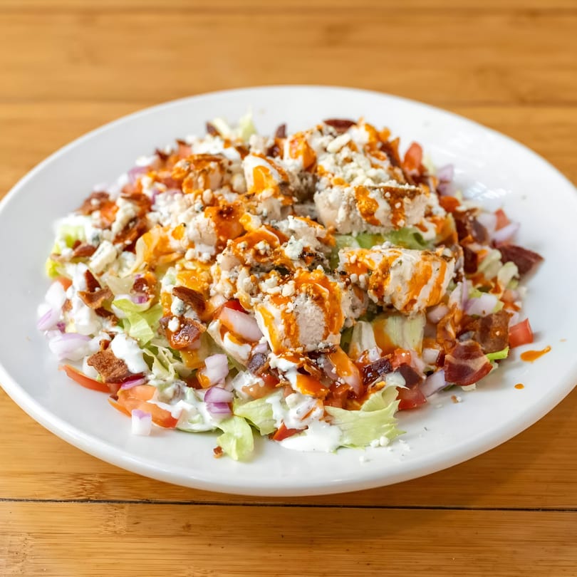 Buffalo chicken salad with bacon, blue cheese, red onion, and tomatoes on a white plate.
