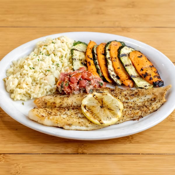 Grilled fish with a lemon slice, rice, grilled zucchini, sweet potatoes, and tomato salsa.
