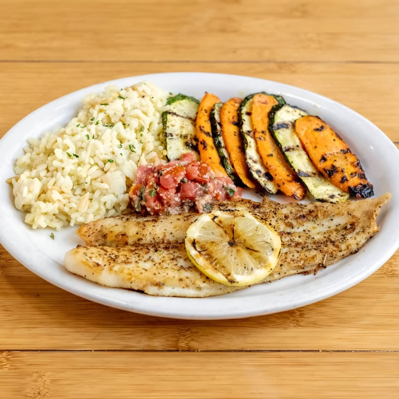 Grilled fish with a lemon slice, rice, grilled zucchini, sweet potatoes, and tomato salsa.