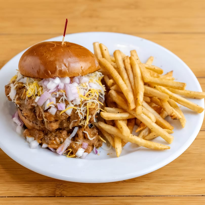 Chili cheeseburger with diced red onions and shredded cheese, served with a side of french fries.