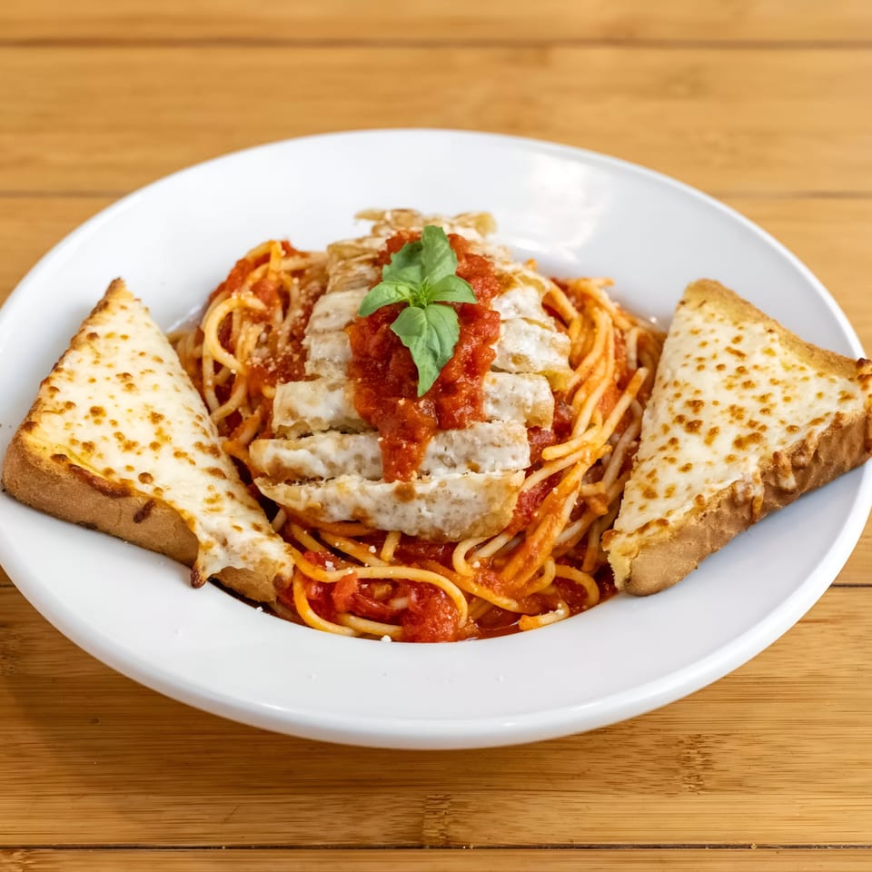 Spaghetti with chicken, marinara sauce, fresh basil, and two slices of cheesy garlic bread.