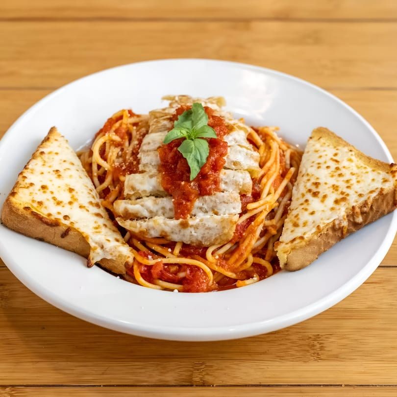 Spaghetti with chicken, marinara sauce, fresh basil, and two slices of cheesy garlic bread.