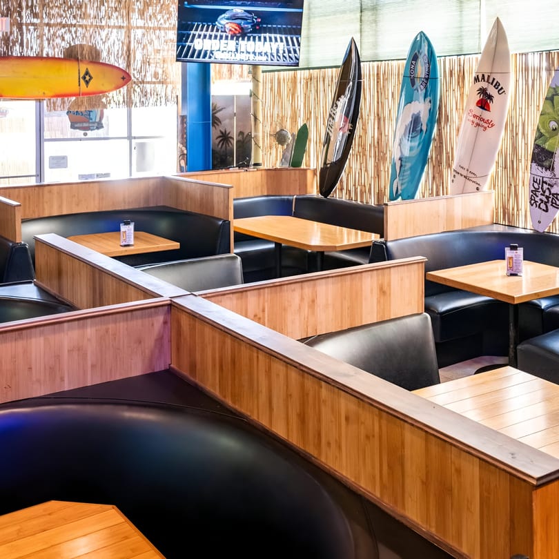 Interior of Beach Sports Grill & Bar with black booths, wooden tables, and surfboards decorating the walls.
